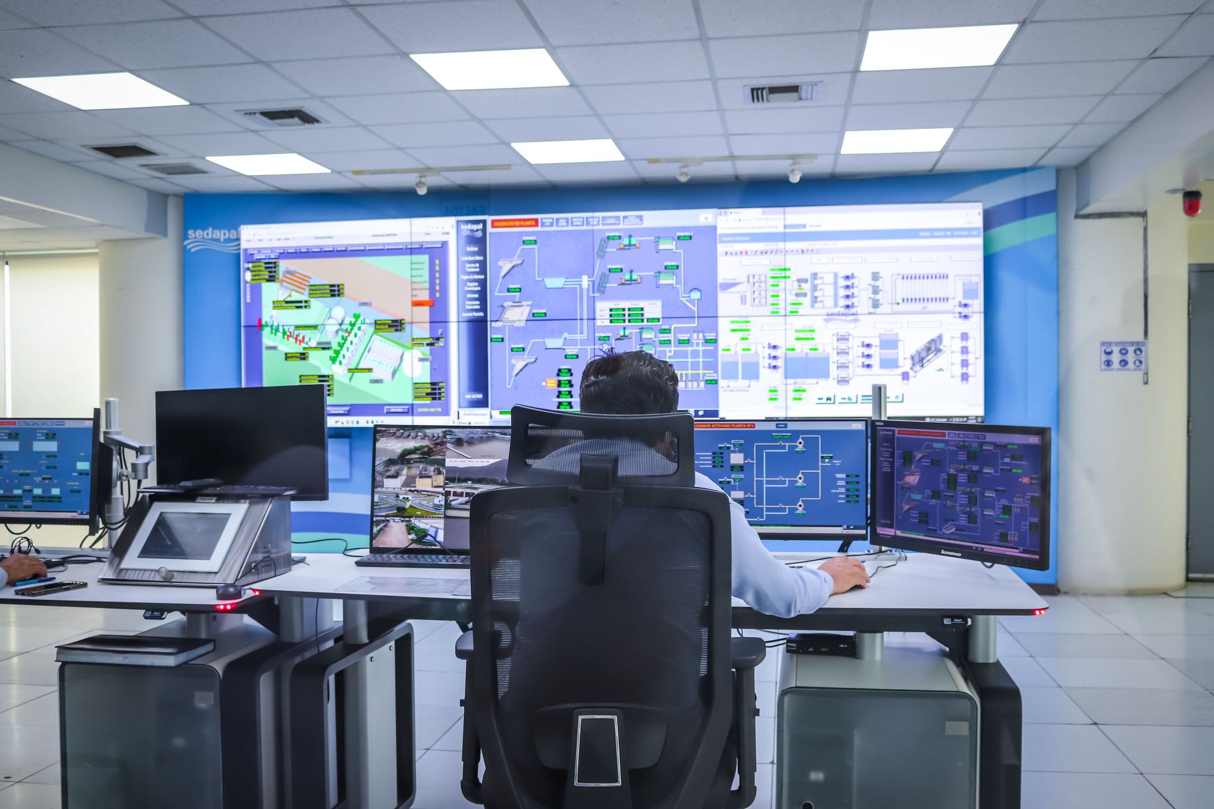 A person working in a control room with a connected system schematic on the wall display